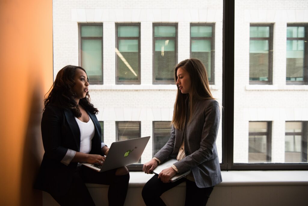 Alt: Two women talking and sitting with a laptop discussing a chief human resources office job description