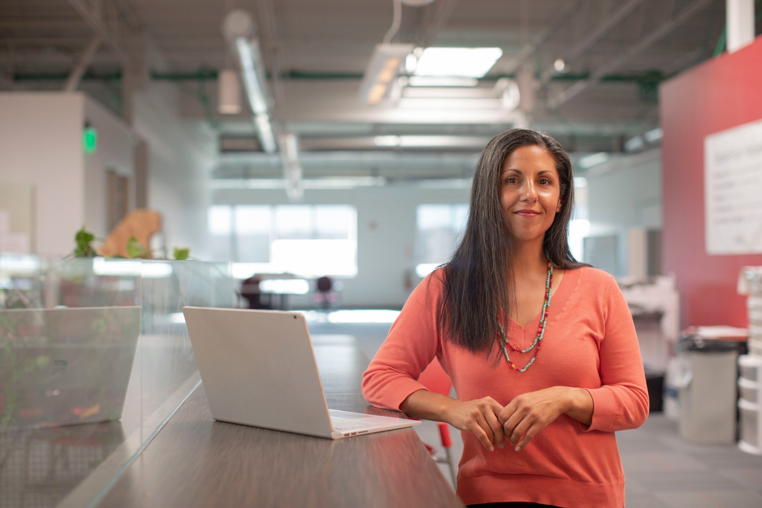 A Woman Standing And Smiling By A Laptop