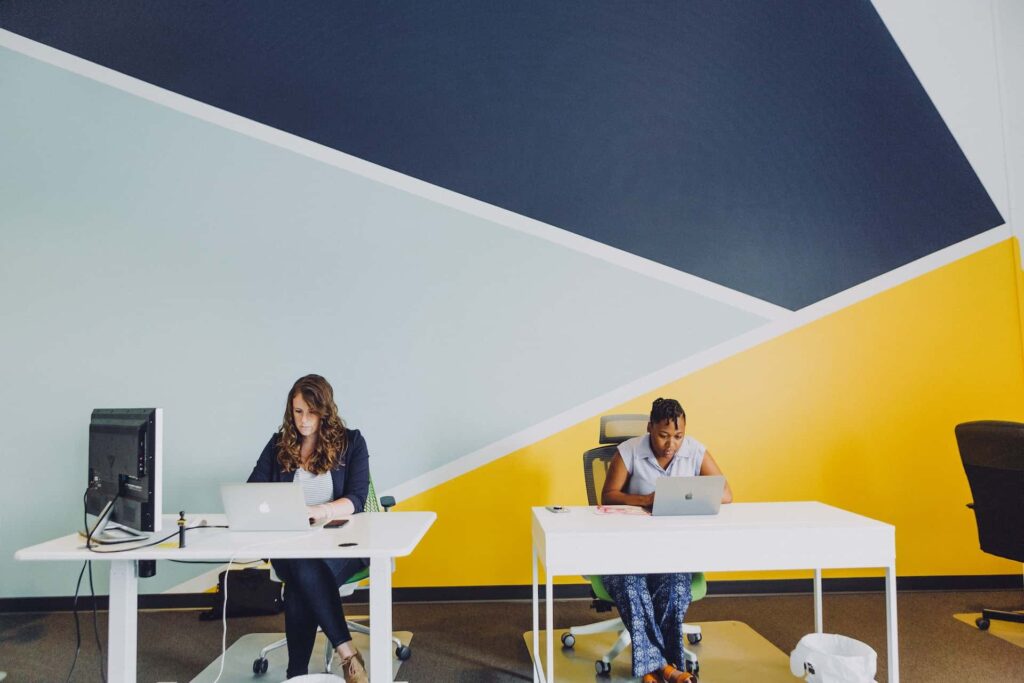 Two labor relations specialists working on laptops on desks in front of a geometric mural