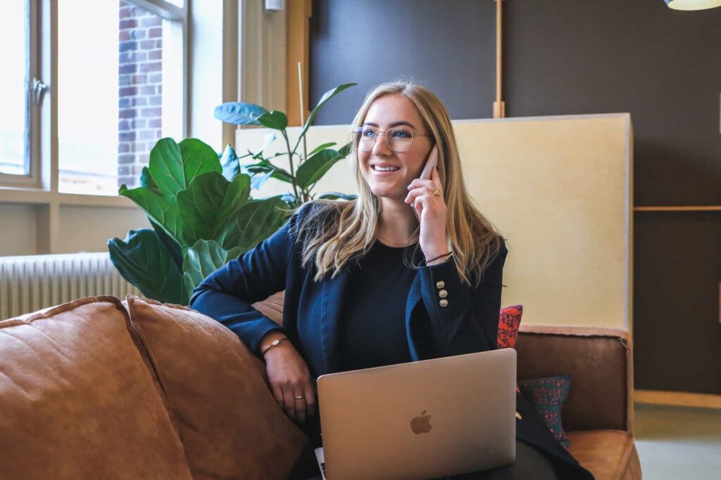 A labor relations specialist talking on the phone sitting on a couch with a laptop