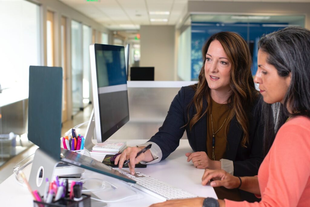 Two women working at a computer reading over a compensation manager job description