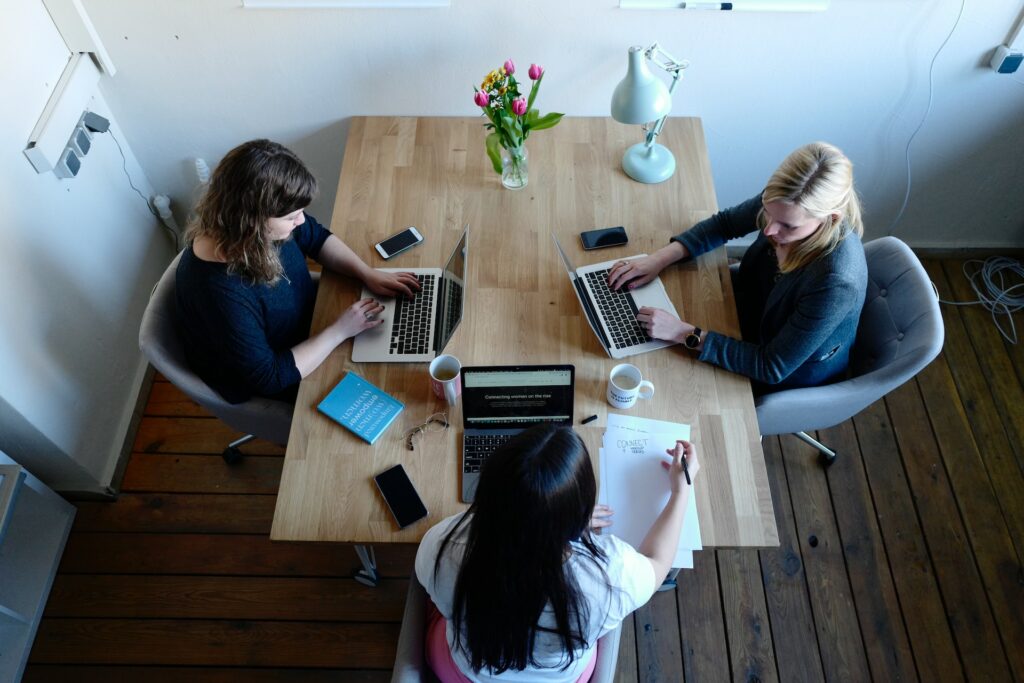 Three women with laptops at a desk reviewing human resource manager education requirements