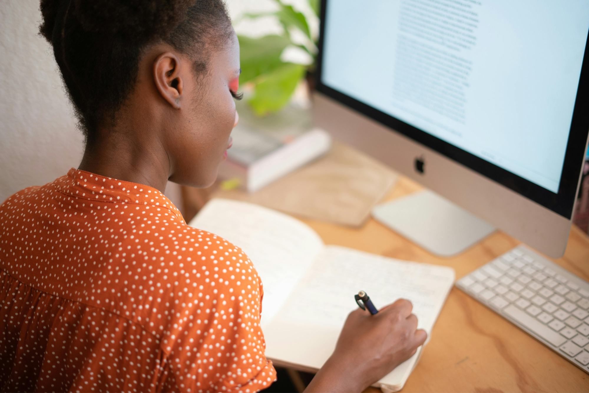 A Woman Taking Notes In A Notebook While Reading Something On Her Computer To Complete Her HR Certifications