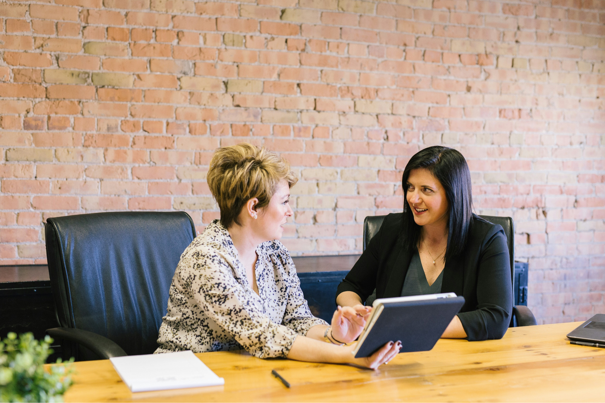 Two Women Speaking In A Workplace About The Future Of HR With A Tablet Between Them