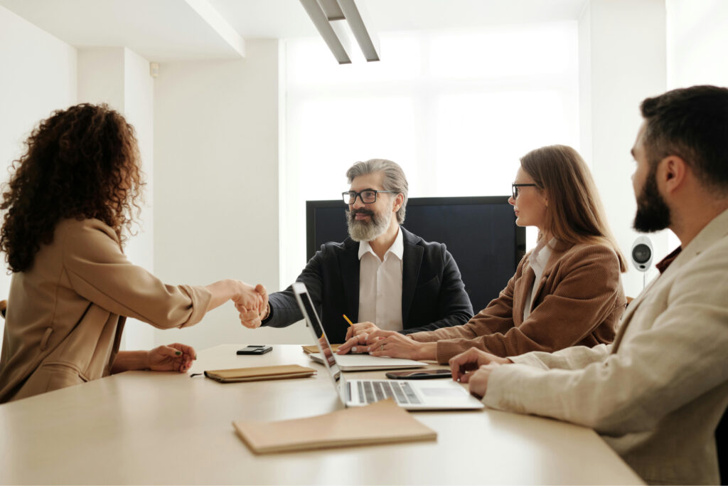 a woman shaking hands with a man sitting beside two other employees during a meeting about HR trends