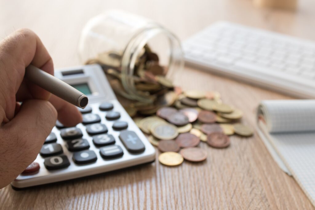 Close-up of a person using a calculator with scattered coins from a jar, representing savings, finance, or budgeting concepts