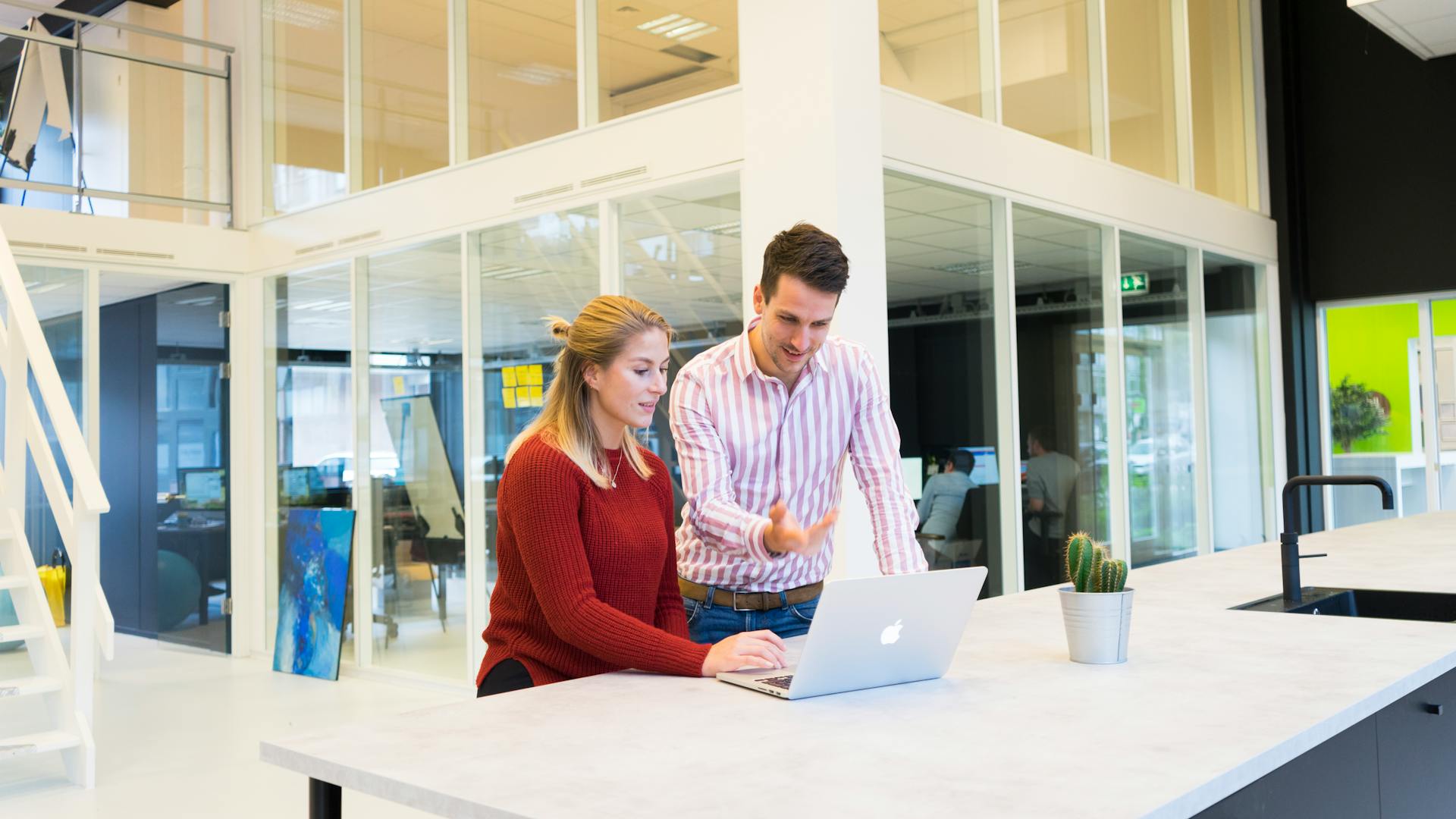 A Man And A Woman Looking Over A Laptop And Conversing At Work
