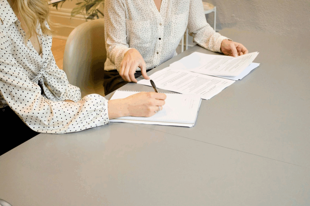 Two women talking about HR manager compensation over a stack of papers